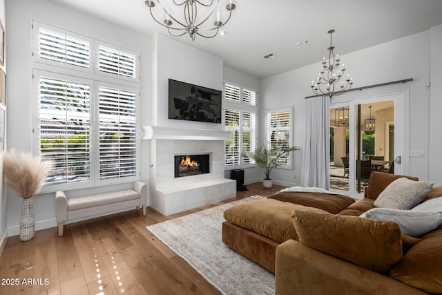 living room featuring a tiled fireplace, a notable chandelier, and light wood-type flooring