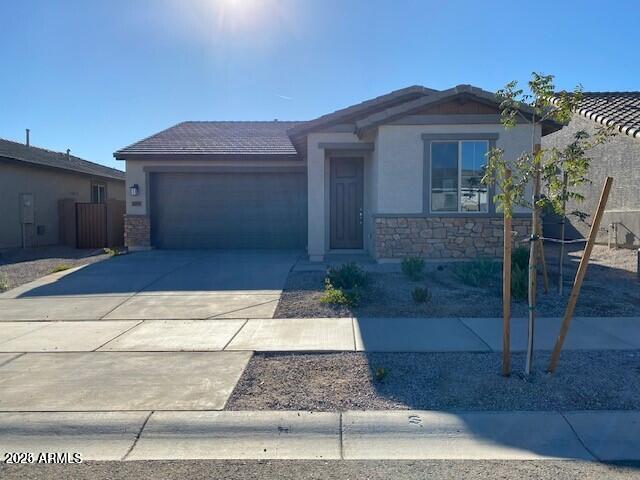 ranch-style home with stucco siding, driveway, stone siding, a garage, and a tiled roof