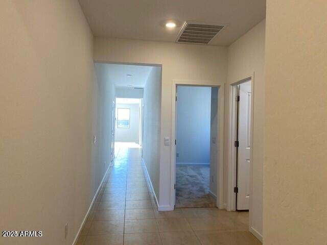 hallway featuring light tile patterned floors, visible vents, and baseboards