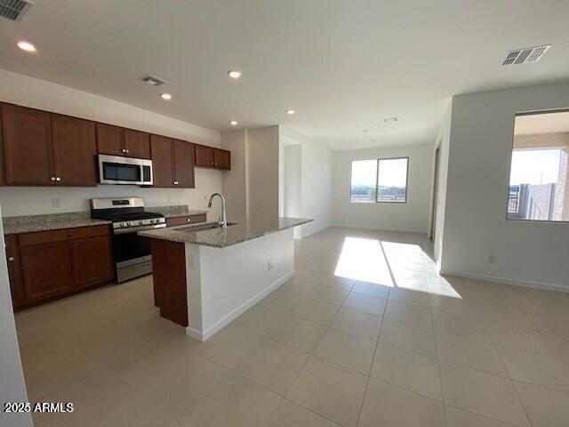 kitchen featuring visible vents, a sink, light stone counters, open floor plan, and stainless steel appliances