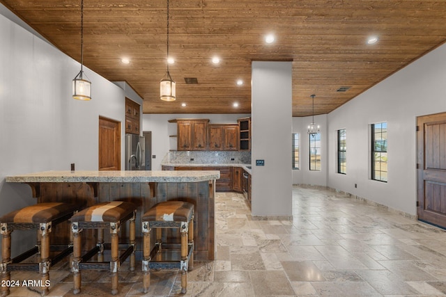 kitchen with backsplash, wood ceiling, a breakfast bar, decorative light fixtures, and stainless steel refrigerator