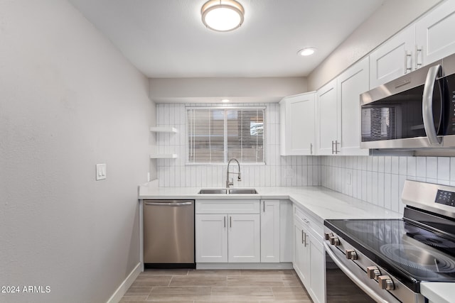 kitchen with white cabinets, backsplash, appliances with stainless steel finishes, light stone countertops, and sink