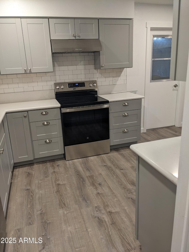 kitchen featuring stainless steel range with electric stovetop, wood-type flooring, gray cabinetry, and wall chimney exhaust hood