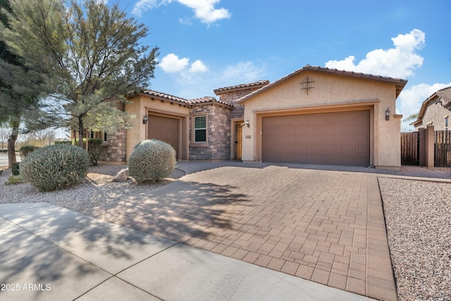 mediterranean / spanish-style house with a garage, a tile roof, stone siding, decorative driveway, and stucco siding