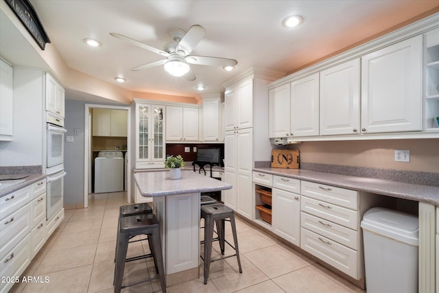kitchen featuring washer / clothes dryer, a breakfast bar area, a ceiling fan, white double oven, and white cabinetry