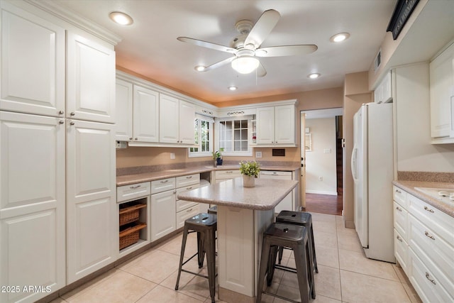 kitchen with freestanding refrigerator, a kitchen bar, white cabinets, a center island, and recessed lighting