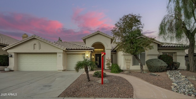 mediterranean / spanish house with a tiled roof, concrete driveway, stucco siding, and an attached garage