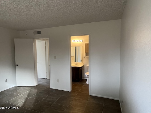 unfurnished bedroom featuring connected bathroom, sink, dark tile patterned floors, and a textured ceiling