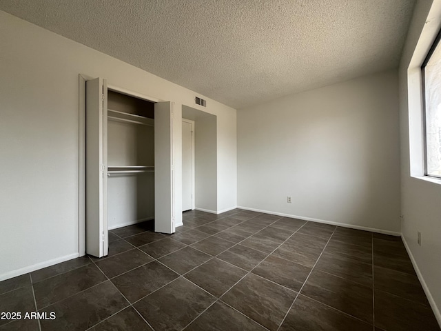 unfurnished bedroom with dark tile patterned flooring, a closet, and a textured ceiling