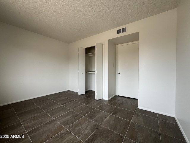 unfurnished bedroom with dark tile patterned floors, a textured ceiling, and a closet