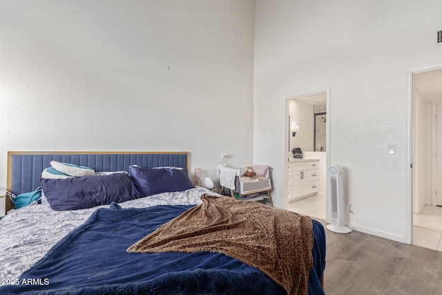 bedroom featuring ensuite bath, wood-type flooring, and a high ceiling