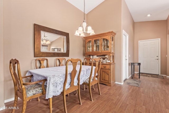 dining space featuring a chandelier, high vaulted ceiling, light wood-style floors, and baseboards