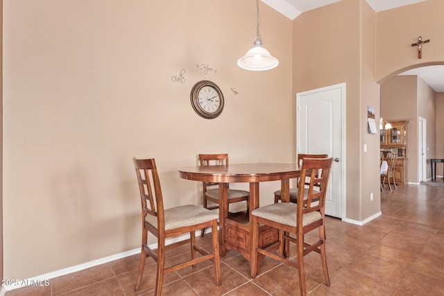 dining area with arched walkways, high vaulted ceiling, tile patterned floors, and baseboards