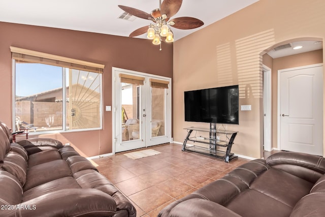 tiled living area featuring baseboards, arched walkways, ceiling fan, and french doors
