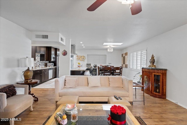 living room featuring ceiling fan, sink, and light wood-type flooring