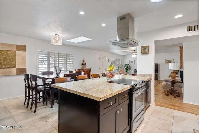 kitchen with island exhaust hood, ceiling fan, light stone counters, dark brown cabinets, and electric stove