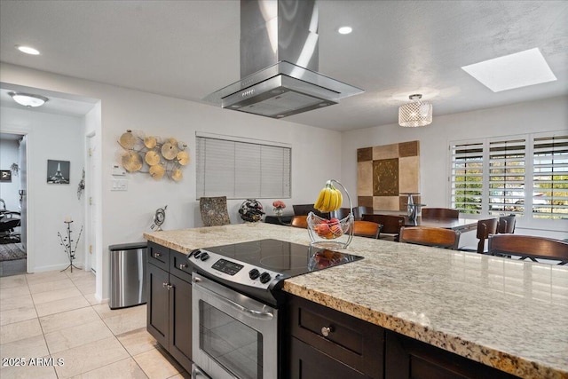 kitchen featuring light tile patterned floors, a skylight, dark brown cabinetry, island range hood, and stainless steel range with electric cooktop