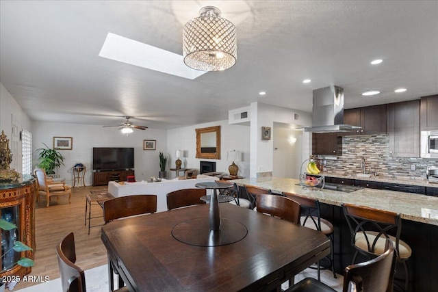 dining room featuring a skylight, sink, ceiling fan, and light hardwood / wood-style flooring