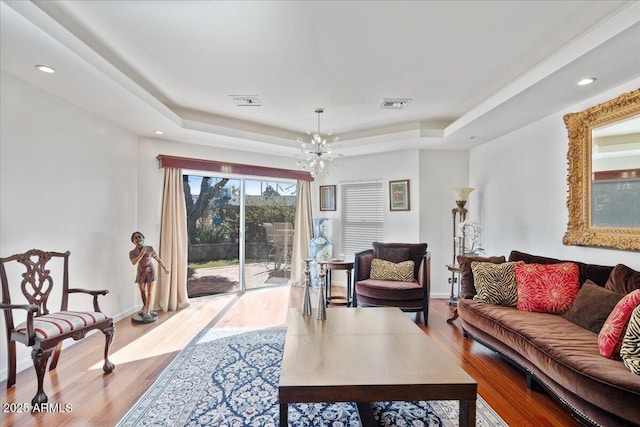 living room featuring an inviting chandelier, a raised ceiling, and light wood-type flooring