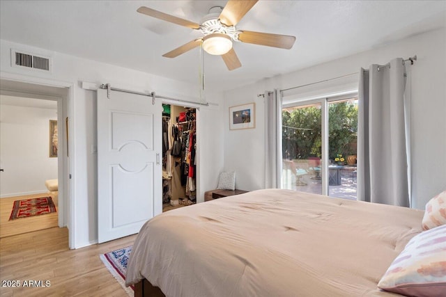 bedroom featuring a spacious closet, ceiling fan, light hardwood / wood-style floors, a barn door, and a closet