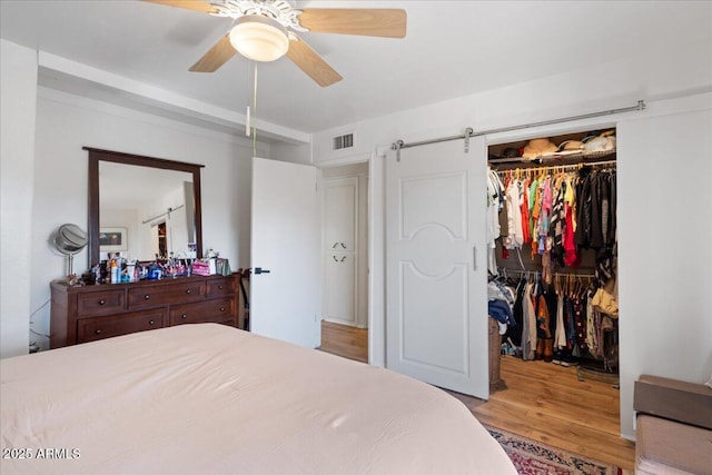 bedroom featuring light hardwood / wood-style flooring, ceiling fan, a barn door, a spacious closet, and a closet