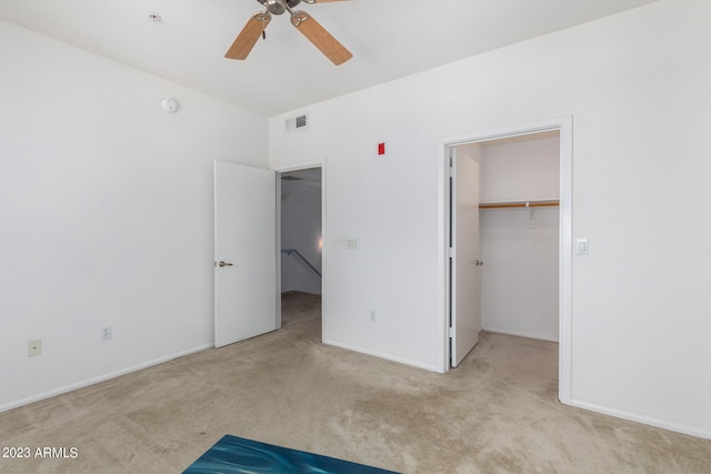 unfurnished bedroom with ceiling fan, light colored carpet, a walk in closet, and a closet