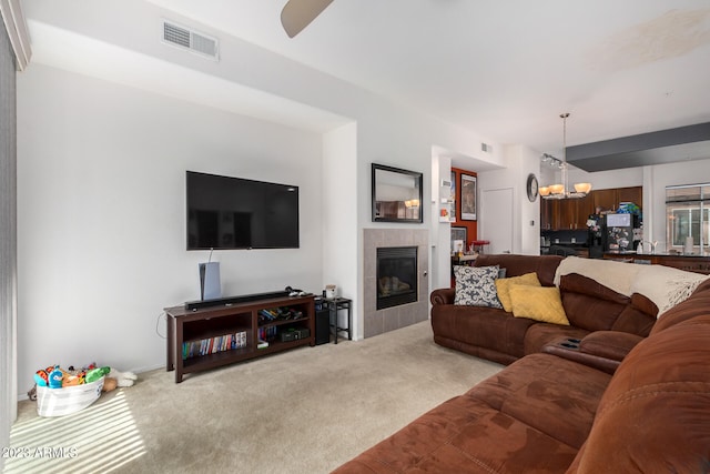 carpeted living room featuring ceiling fan with notable chandelier and a tiled fireplace