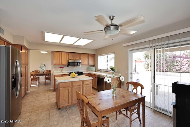 kitchen with tile countertops, light tile patterned floors, stainless steel appliances, a kitchen island, and a sink