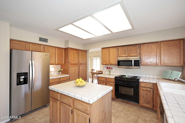 kitchen featuring visible vents, tile countertops, a kitchen island, appliances with stainless steel finishes, and a sink