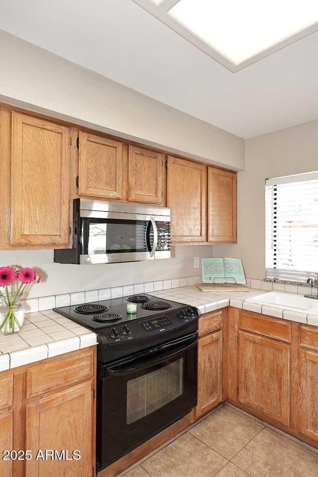 kitchen with stainless steel microwave, black range with electric stovetop, tile countertops, and a sink