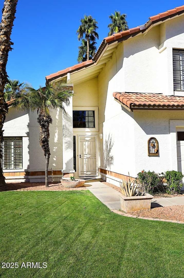 view of exterior entry with a tile roof, a yard, and stucco siding