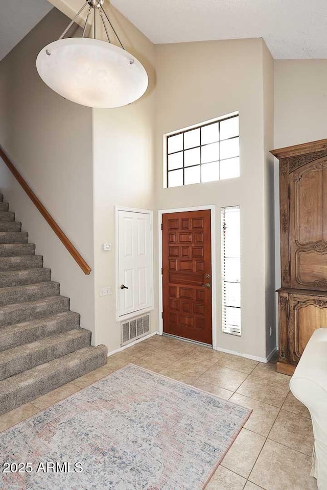 entrance foyer with visible vents, stairway, light tile patterned flooring, high vaulted ceiling, and baseboards