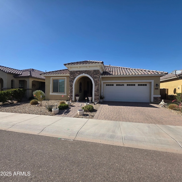 mediterranean / spanish-style home featuring stucco siding, decorative driveway, stone siding, an attached garage, and a tiled roof