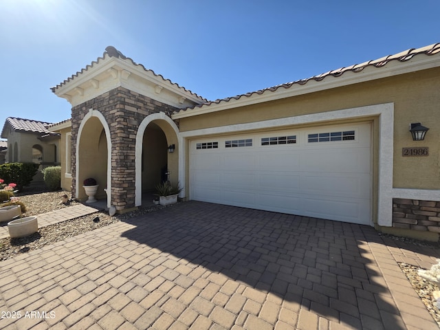 view of front of house with a tiled roof, decorative driveway, a garage, and stucco siding