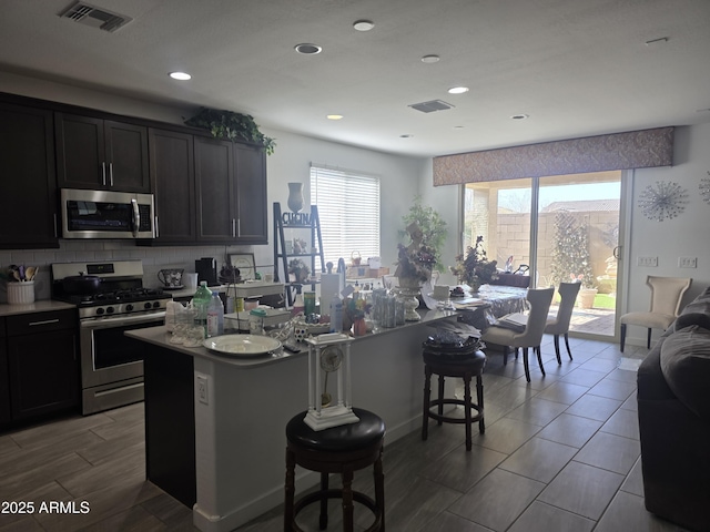 kitchen with visible vents, a breakfast bar, stainless steel appliances, decorative backsplash, and a center island