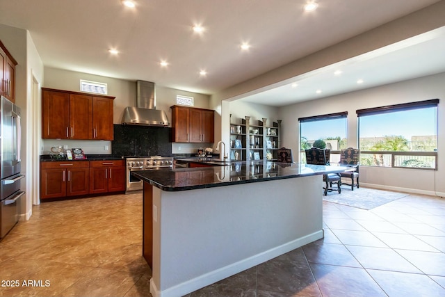 kitchen with a center island with sink, decorative backsplash, stainless steel appliances, wall chimney range hood, and a sink