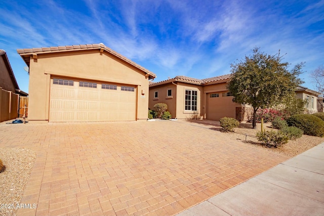 mediterranean / spanish-style home featuring an attached garage, a tiled roof, decorative driveway, and stucco siding