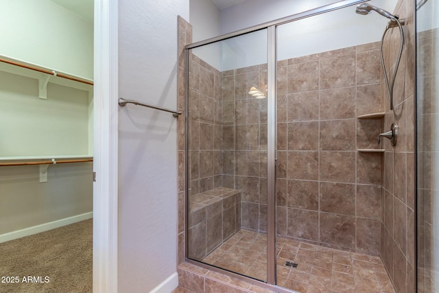 bathroom with a stall shower, a walk in closet, and baseboards