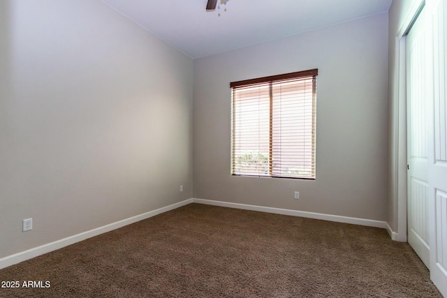 empty room with a ceiling fan, vaulted ceiling, dark carpet, and baseboards