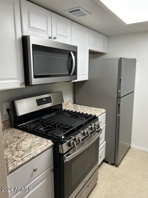 kitchen with light stone countertops, light tile patterned floors, appliances with stainless steel finishes, tasteful backsplash, and white cabinetry