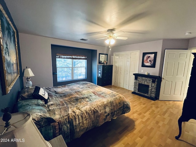 bedroom featuring wood finished floors, visible vents, a fireplace, ceiling fan, and a closet