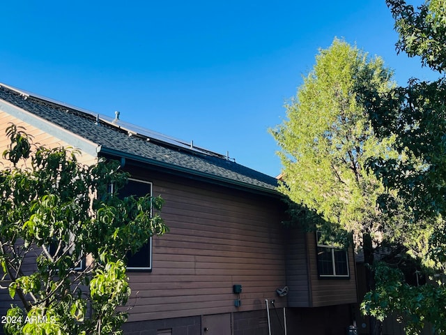 view of property exterior featuring roof mounted solar panels and roof with shingles