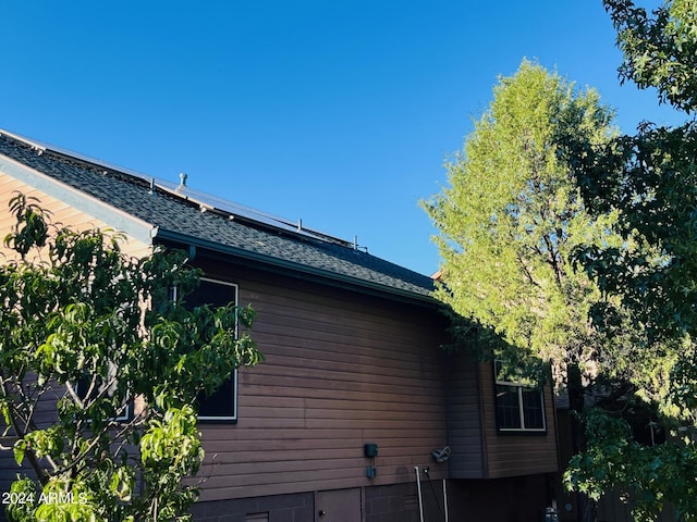 view of property exterior with roof mounted solar panels and roof with shingles