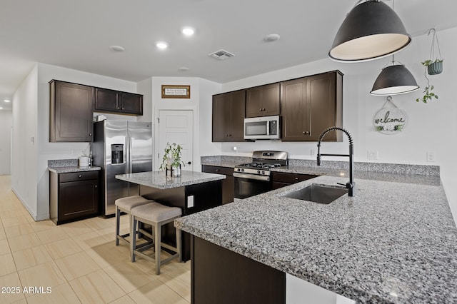 kitchen featuring appliances with stainless steel finishes, sink, a breakfast bar area, hanging light fixtures, and light stone countertops