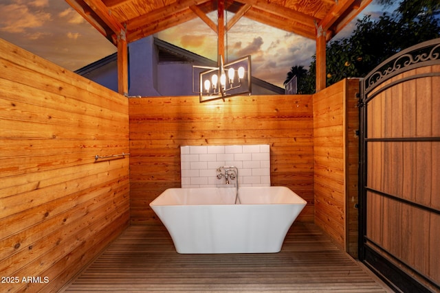 bathroom with vaulted ceiling with beams, a washtub, a notable chandelier, and wooden walls