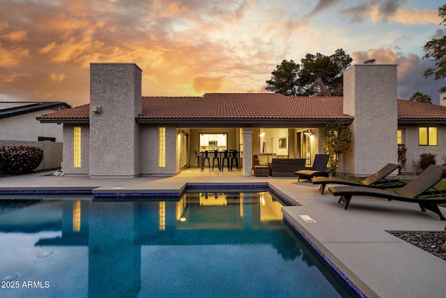 pool at dusk with a patio area, outdoor lounge area, and exterior bar