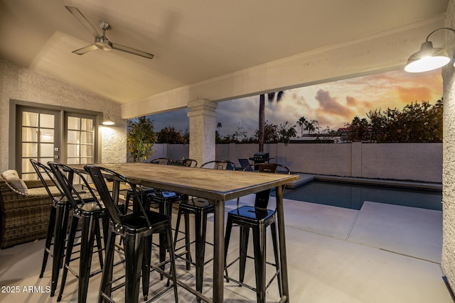 patio terrace at dusk featuring a fenced in pool and ceiling fan