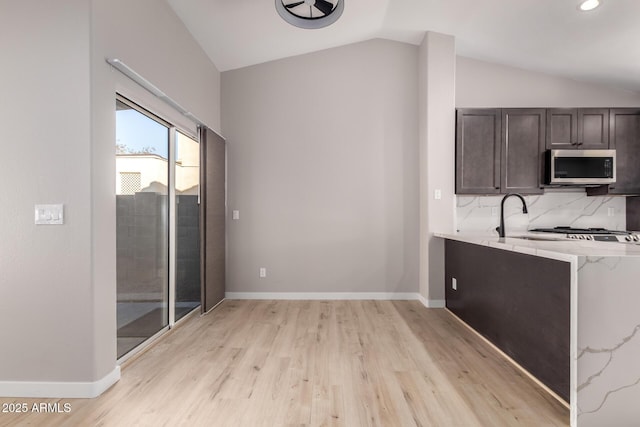 kitchen with dark brown cabinetry, lofted ceiling, light hardwood / wood-style floors, and decorative backsplash