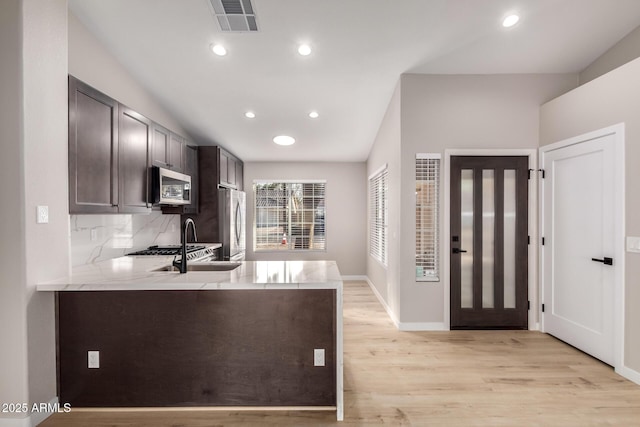 kitchen featuring appliances with stainless steel finishes, decorative backsplash, light wood-type flooring, and kitchen peninsula