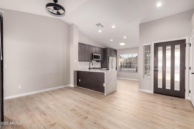 kitchen with stainless steel appliances, vaulted ceiling, dark brown cabinets, and light hardwood / wood-style flooring